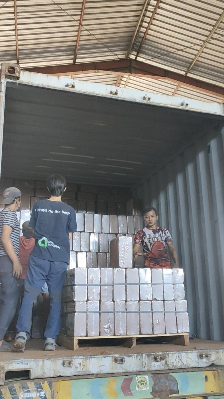 Two Agrorise Indonesia team members floor loading wrapped bales by hand inside a container.