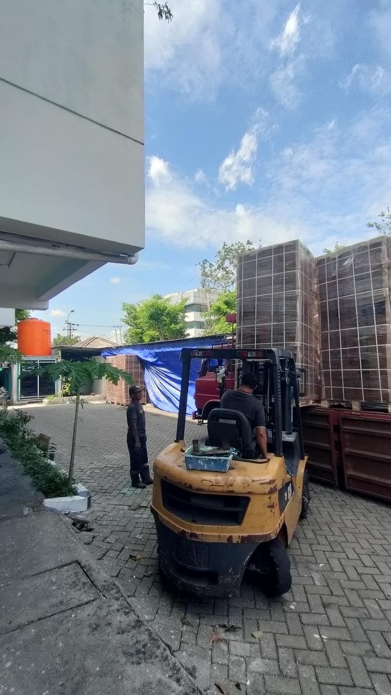 Forklift carrying a wrapped pallet of cocopeat blocks across the yard towards waiting containers.