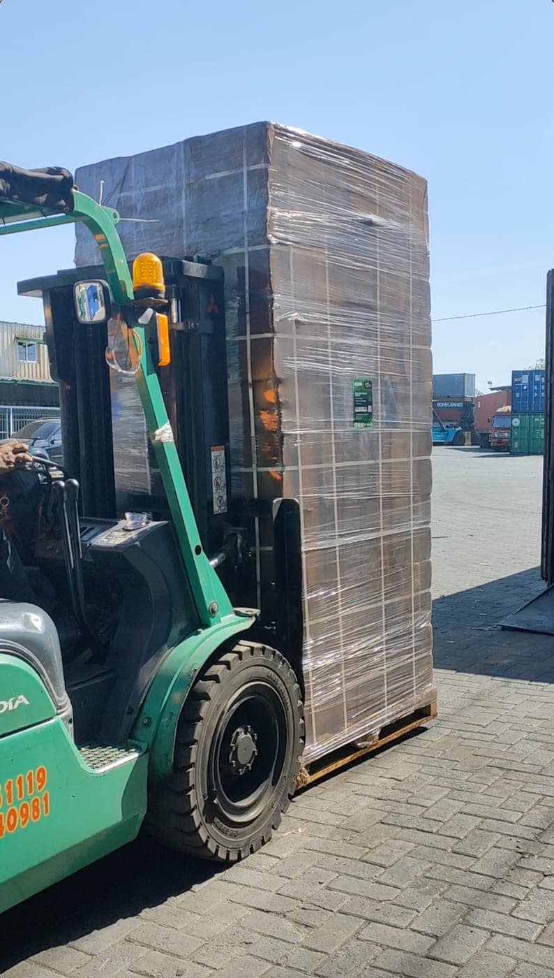 Green forklift carrying a wrapped pallet of cocopeat blocks towards the container yard.