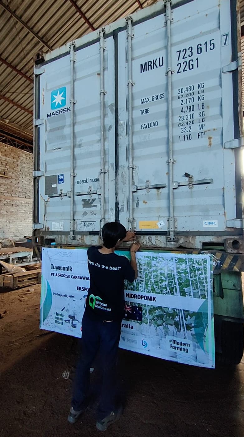 Loaded container at the shed with an Agrorise Indonesia team member holding a printed product board alongside.