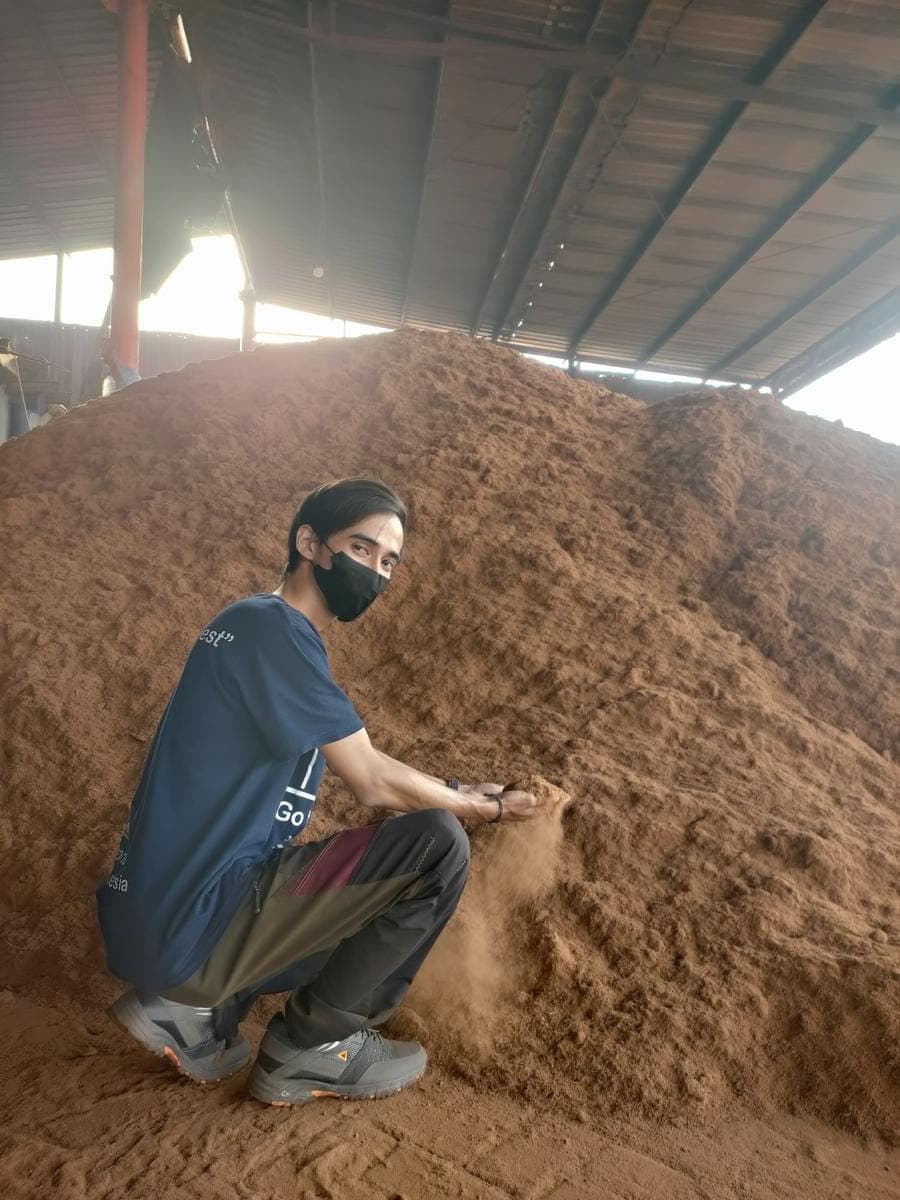Agrorise Indonesia team member kneeling beside a large indoor pile of loose cocopeat.