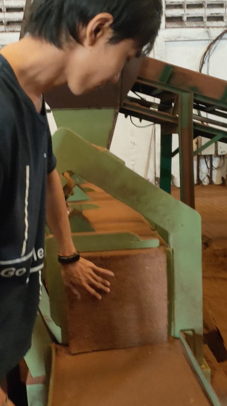 أحد أفراد فريق Agrorise Indonesia يغذي الكوكوبيت في قالب مكبس الضغط.