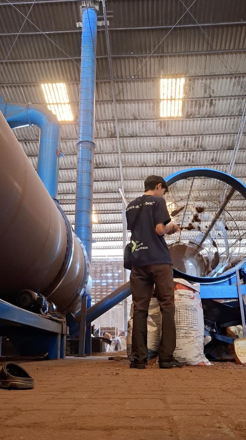 Agrorise Indonesia team member at a drying drum inside a covered processing area.