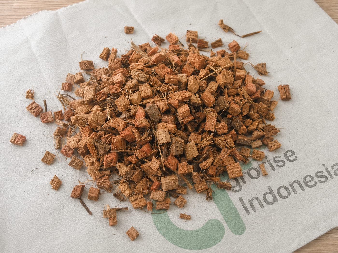 Loose coco husk chips in a larger chip size, spread on an Agrorise Indonesia canvas sack.