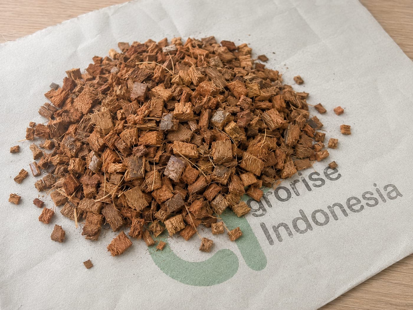 Loose coco husk chips in a medium chip size, spread on an Agrorise Indonesia canvas sack.