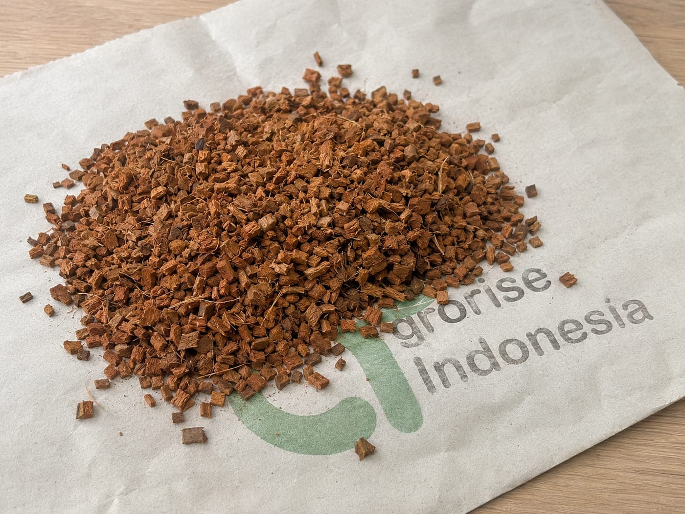 Loose coco husk chips in a smaller chip size, spread on an Agrorise Indonesia canvas sack.