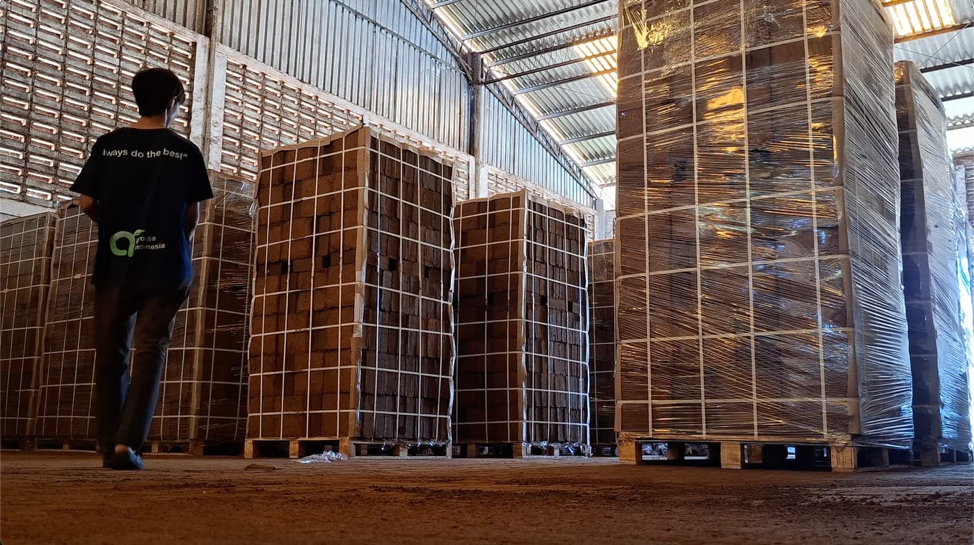 Agrorise Indonesia team member walking along an aisle of stacked cocopeat block pallets.