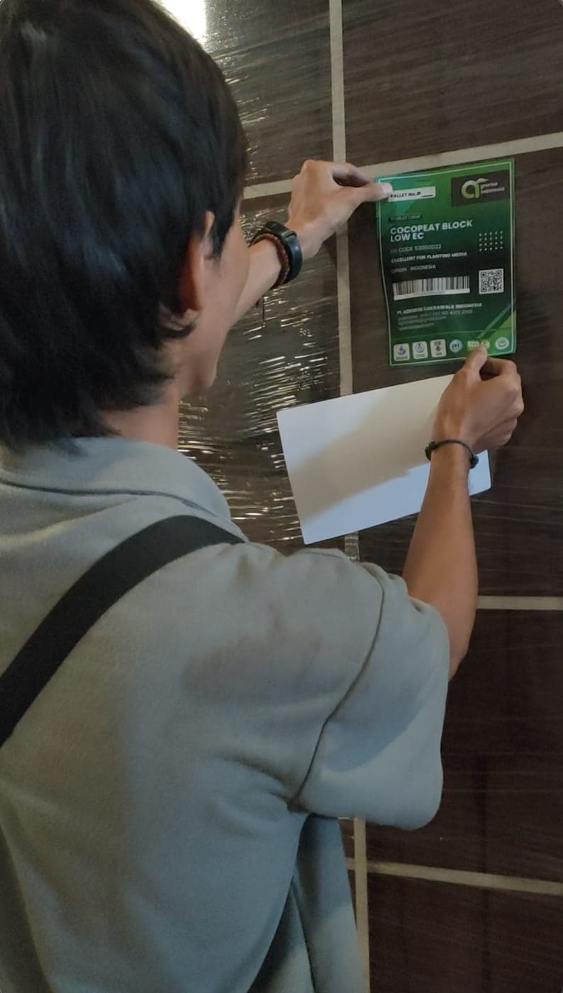 Agrorise Indonesia team member attaching a printed product marking card to a wrapped pallet.